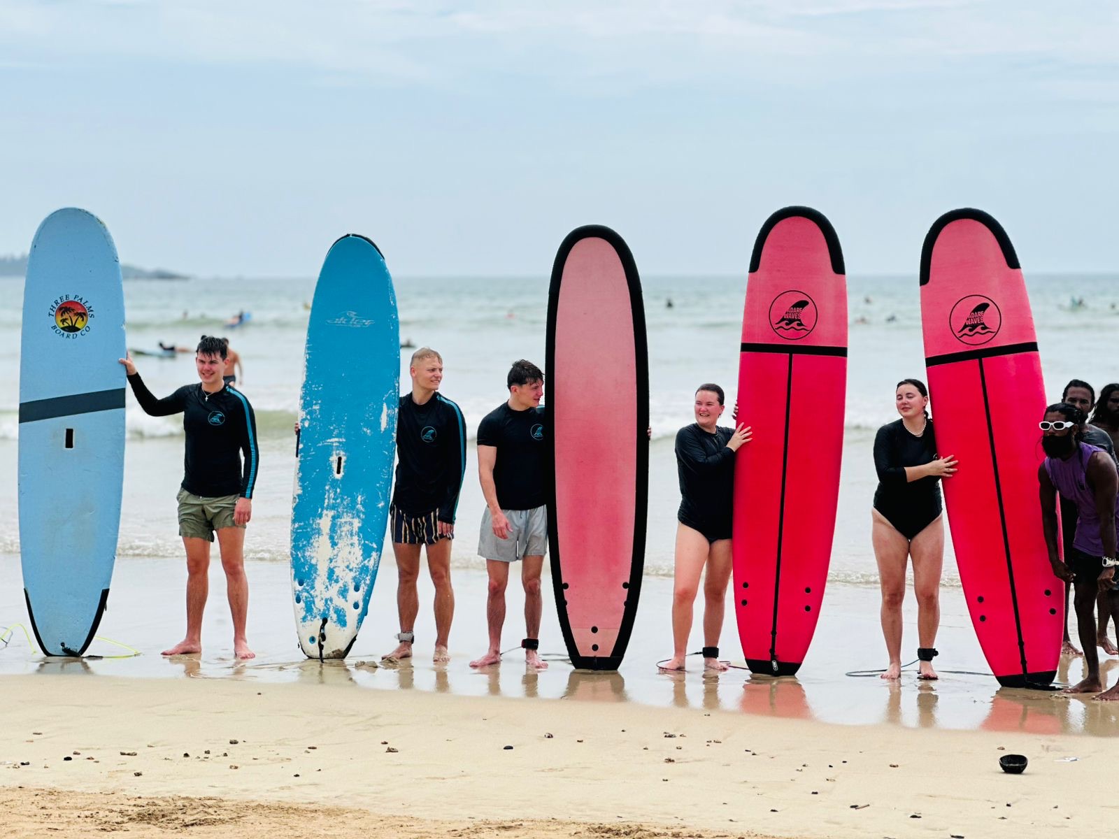 A group of surfers standing beside colourful boards at the shoreline