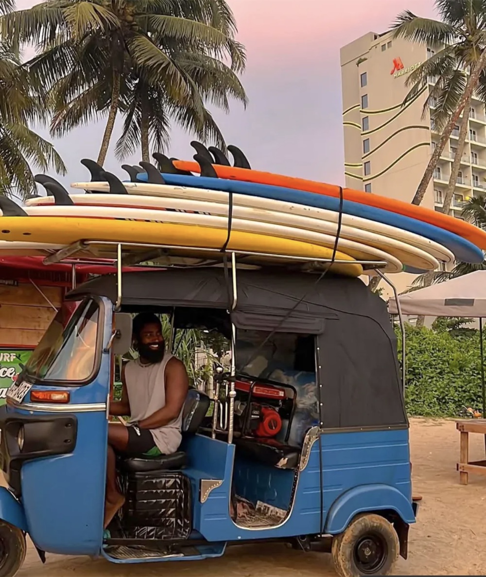 Lahiru driving a blue tuk-tuk loaded with colourful surfboards toward Weligama beach early in the morning