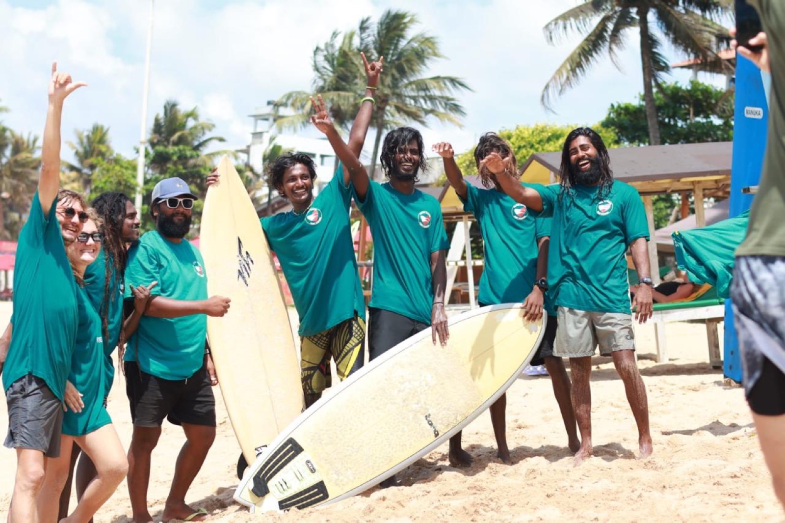 Lahiru and the Adare Waves instructor crew smiling with surfers and boards on Weligama beach