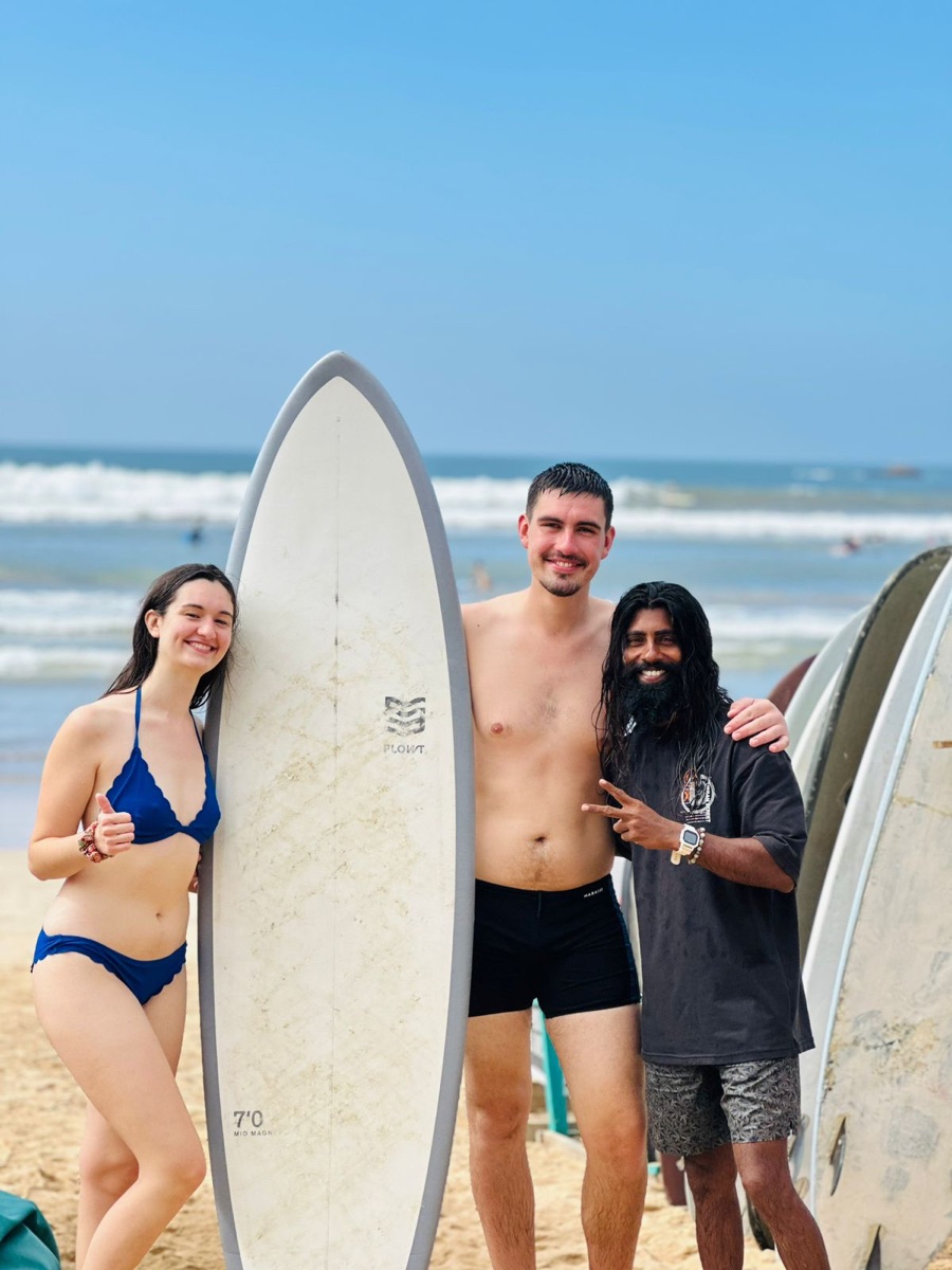 Two smiling surf students standing with Lahiru after a Weligama lesson