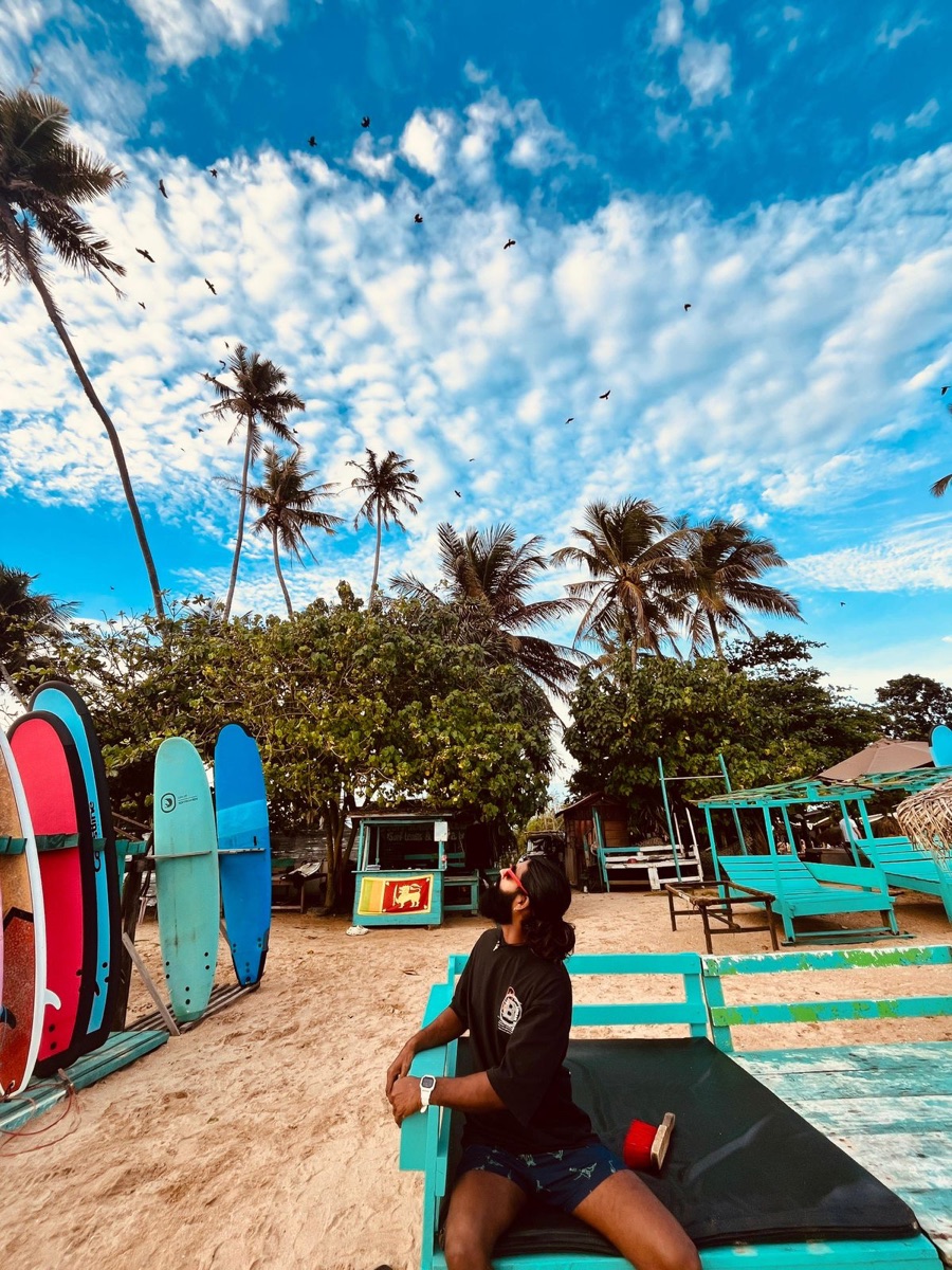 Lahiru relaxing beside colourful surfboards at the beach school